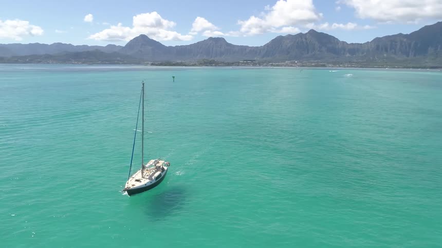 A sailboat gracefully glides along beautiful clear waters near a tropical coastline