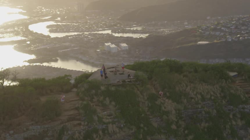 People standing and sitting on a high hilltop clearing overlooking the water and buildings below