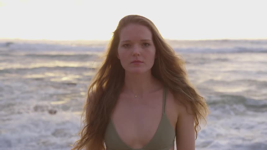 A woman standing on a beach staring with the ocean and the sky in the background