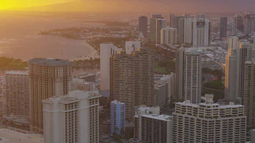 Sunrise over the ocean glows yellow on a coastal citys buildings and skyscrapers