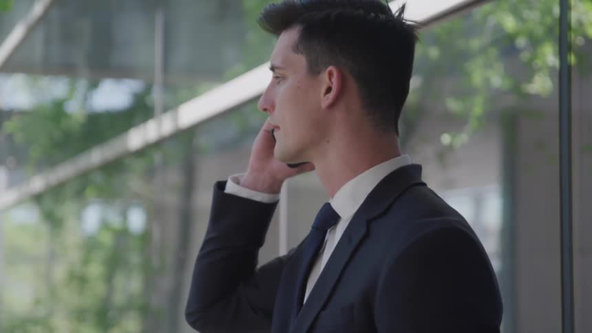 Man holds a cellphone to his ear as he stands near the trees