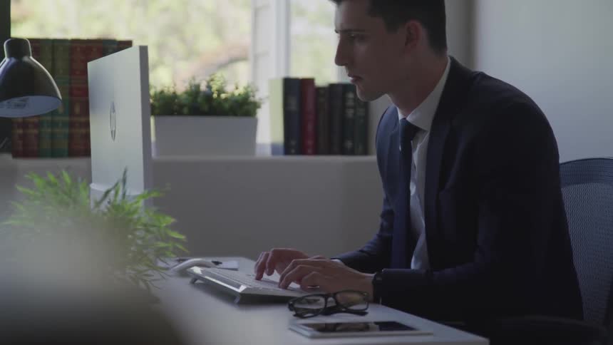 Businessman wearing a suit sits at the desk and types on the keyboard in the office
