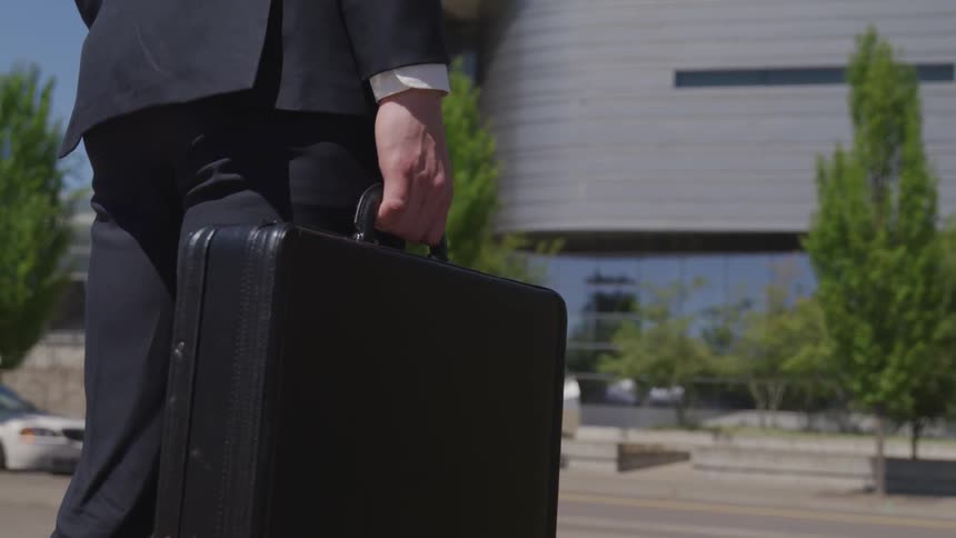 A man in a suit stands outdoors holding a briefcase