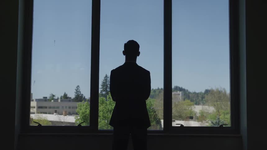 A man is looking out the window in the dark room