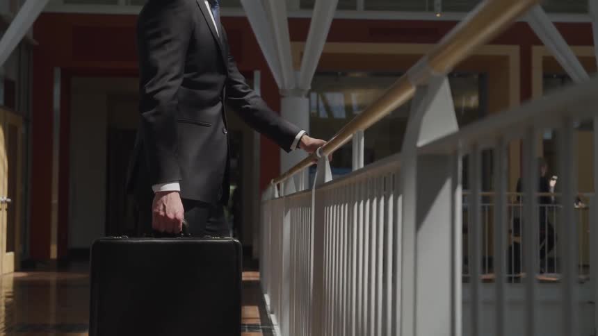 Man holds onto a briefcase with one hand as he holds on to a railing with the other