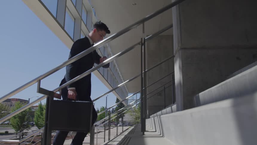 A man in a suit carrying a briefcase walks up stairs and looks at his watch