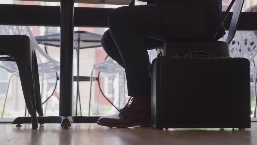 A briefcase stands on the floor next to a man sitting at a cafe table