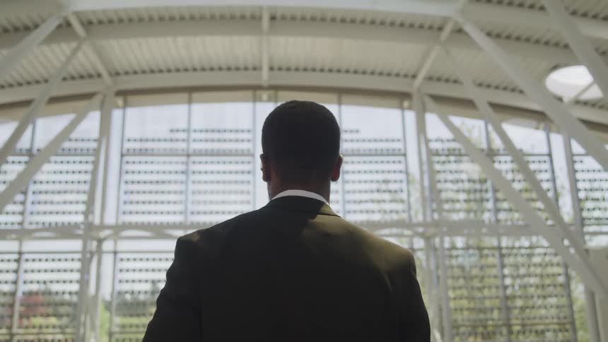 African american man in a business suit standing looking out a large office window
