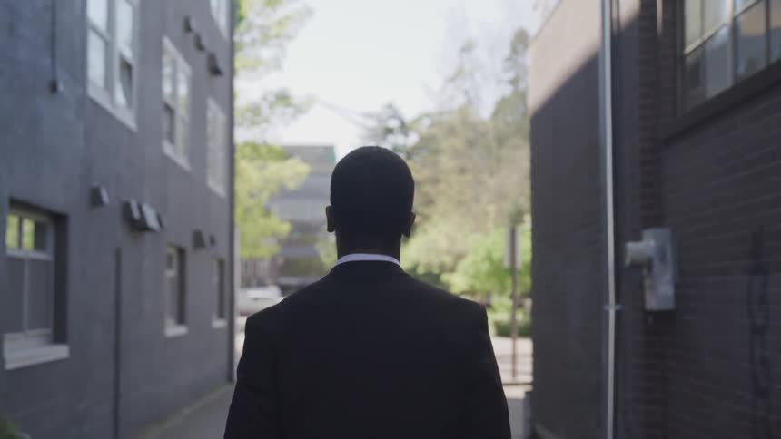 A black man walks between two buildings