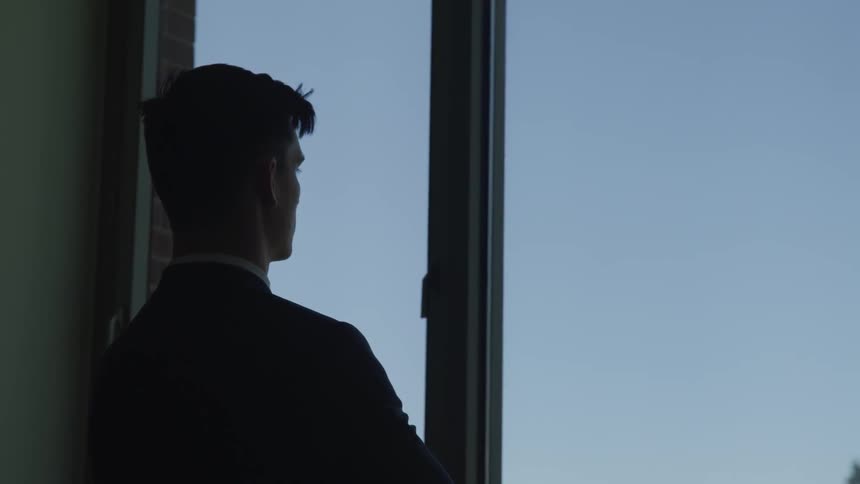 A silhouette of a man with suit looking through the window