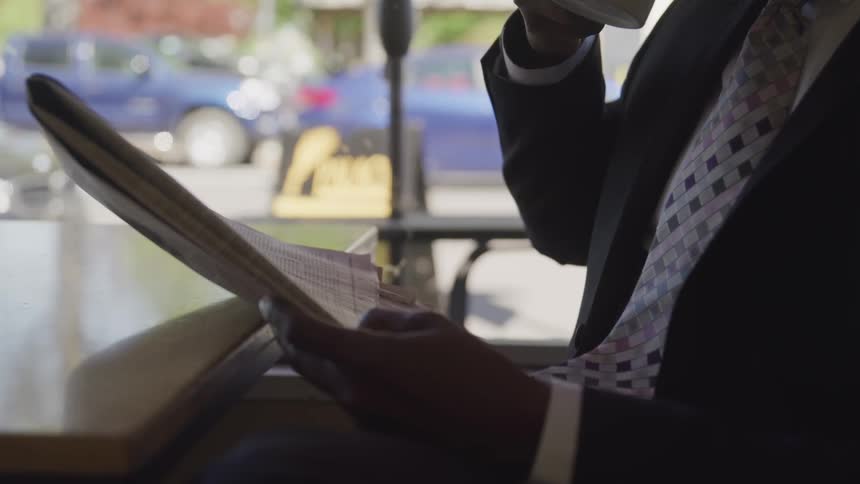 Business man sitting near a window drinking coffee and reading a newspaper