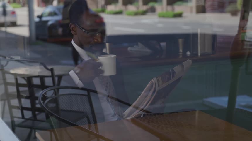 A man reads a newspaper while drinking coffee at a coffee shop