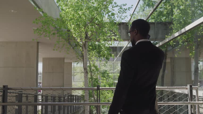 A man with a suit walking back and forth and talking on a smartphone