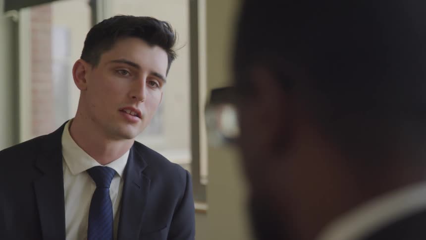 White businessman looks at the black businessman sitting at the table in the office