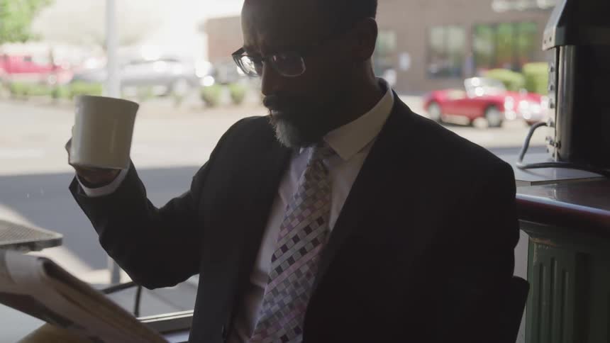 A man is drinking coffee and reading a newspaper