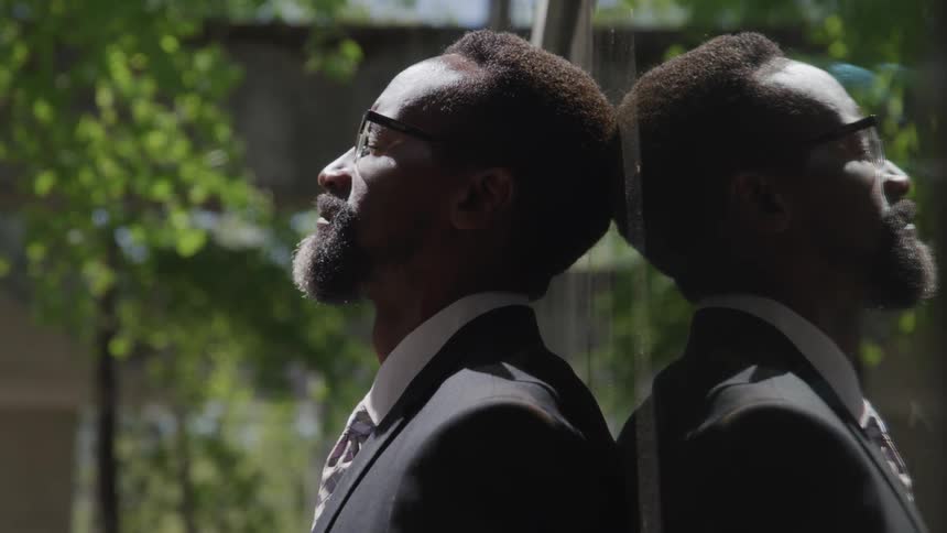 A black man leans his head against a window