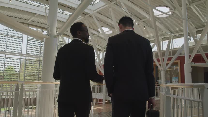 Two businessmen chat while walking through a building