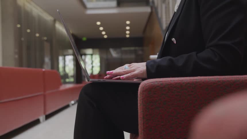 Business woman sitting on the chair uses the laptop on her lap in the office