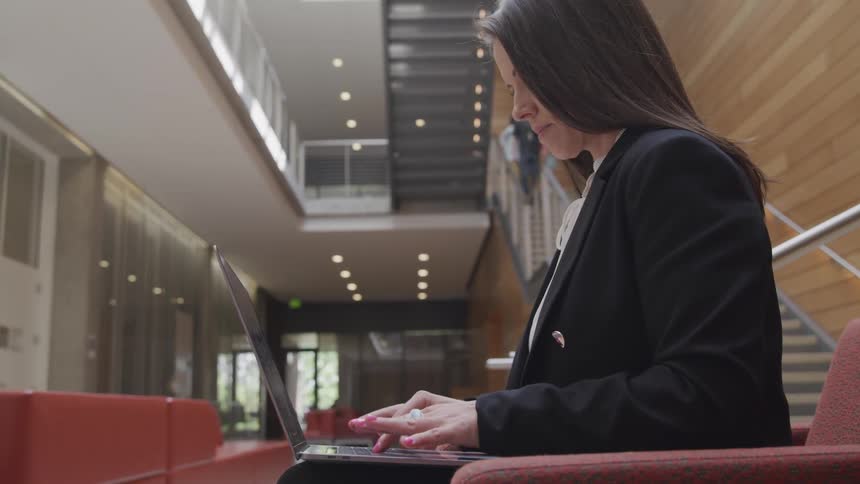 Businesswoman sitting on the chair uses laptop on her lap in the waiting room of the office