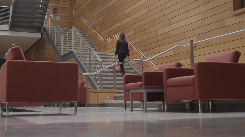 A woman in business attire walks up a set of stairs in a large modern looking building lobby
