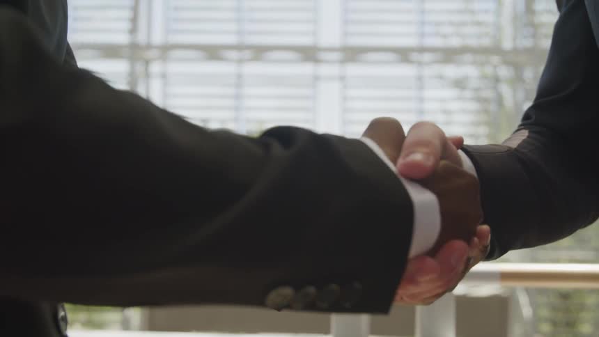 Two businessmen wearing suits shake hands in the office