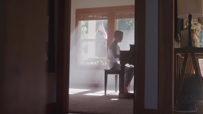 Boy plays the piano while the sun streams through the window