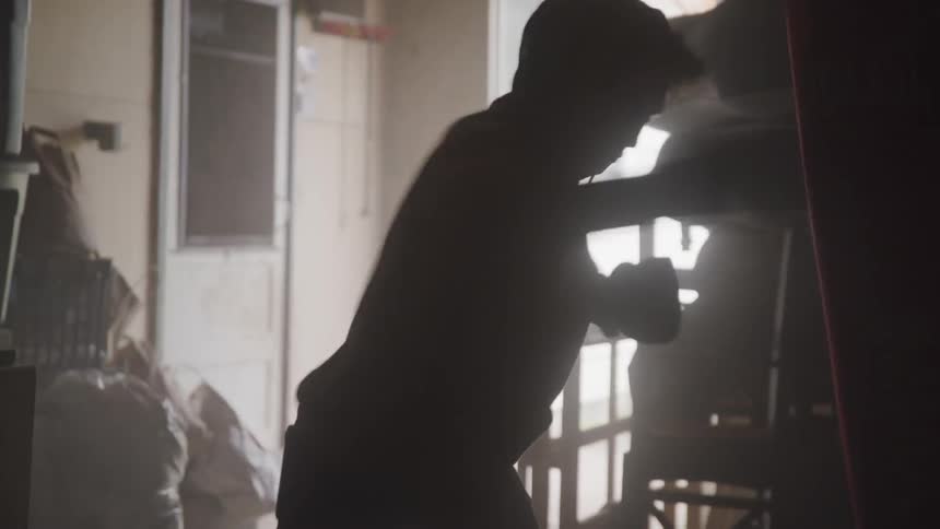 Mans silhouette hits the heavy bag indoors during daylight