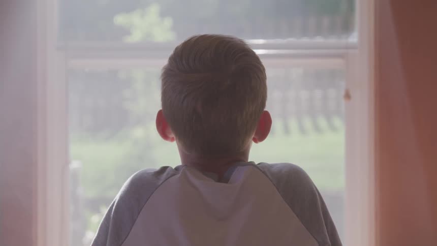 A boy is staring out a window