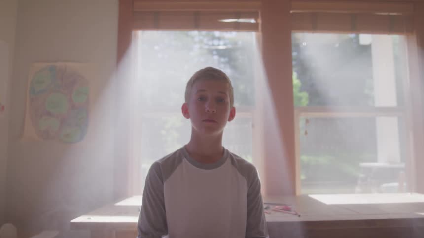 Boy stands near large table surrounded by sunshine from windows