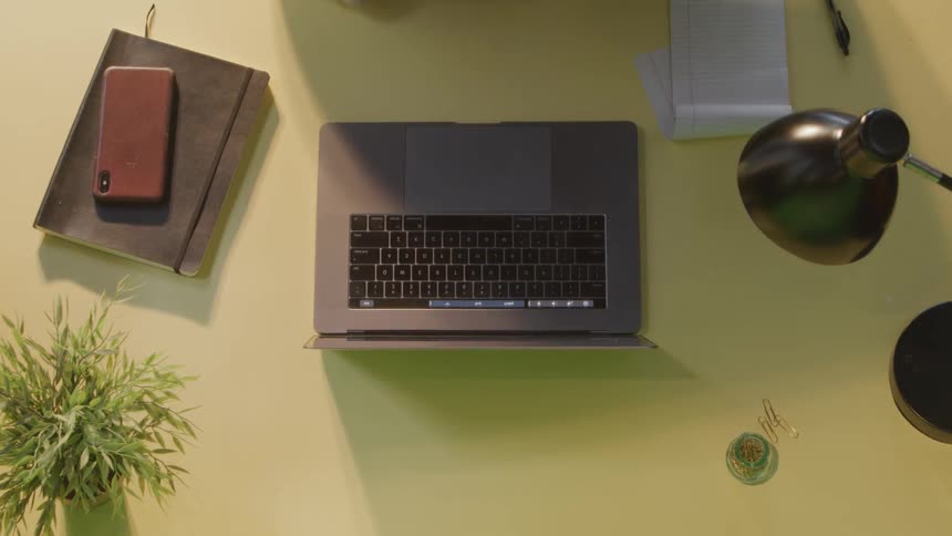 Woman sitting at the yellow table uses laptop and writes down on the notebook in the office