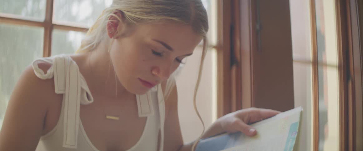 A young woman is reading a book with a window just behind her