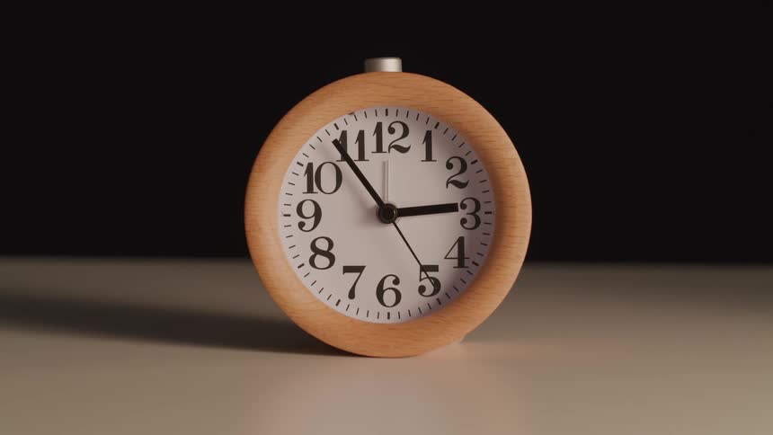 A clock with a wooden frame resting on a brown table with a black background