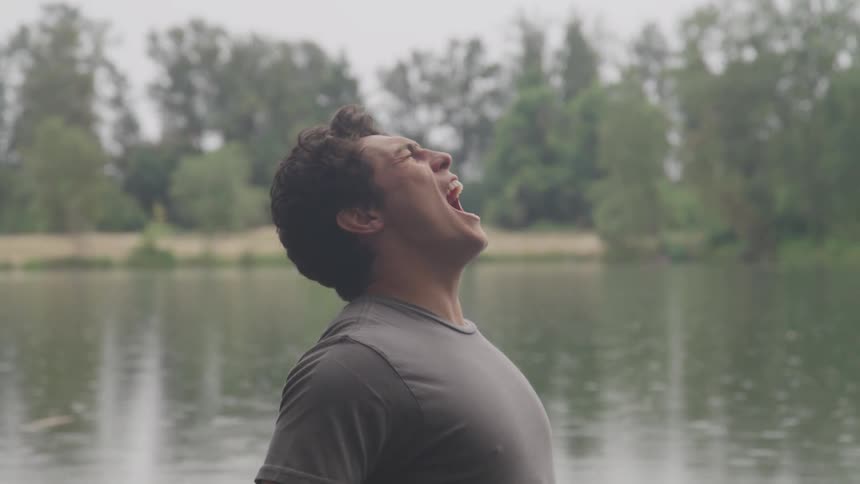 Man screams next to the lake while it drizzles in the forest