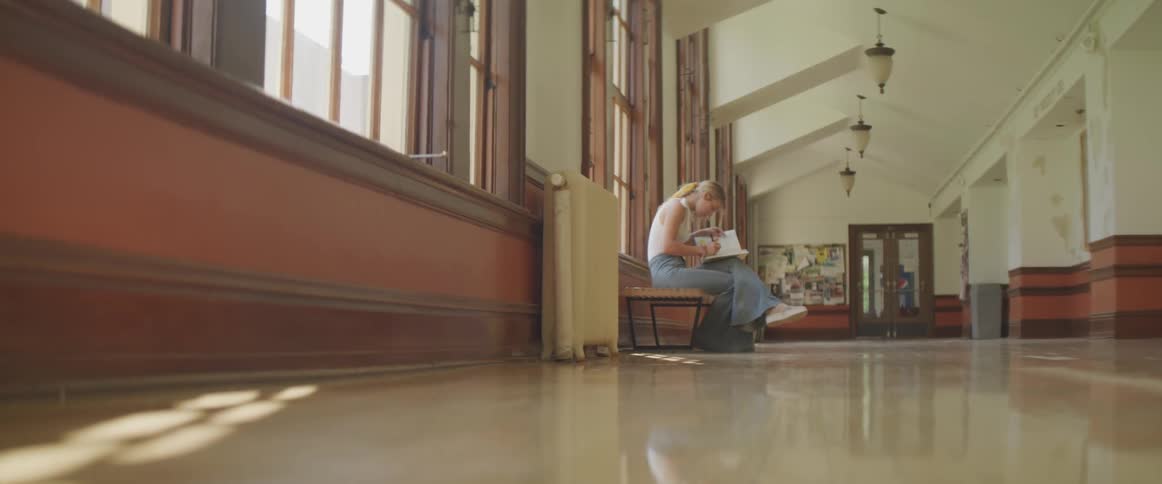 A woman sitting on a bench in a hallway writing in a notebook