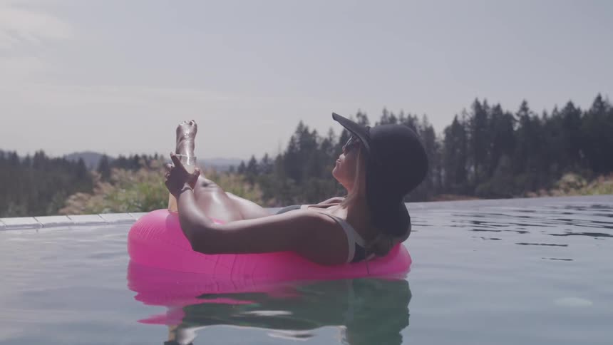 A woman floats in a pool while holding a beverage