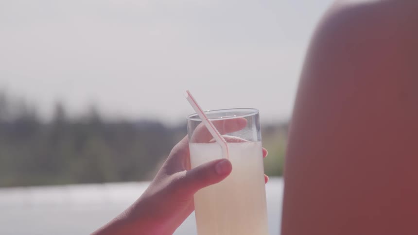 A woman relaxes with a drink while floating on an inflatable ring in an infinity pool
