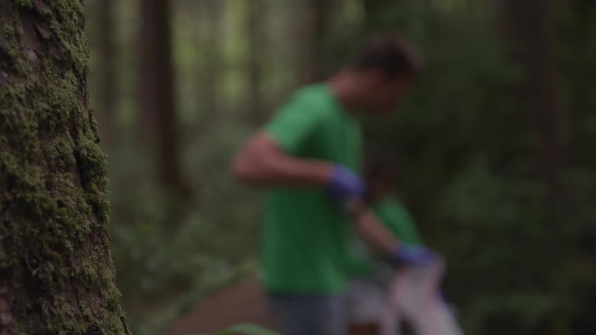 A man and woman pick up garbage in the woods