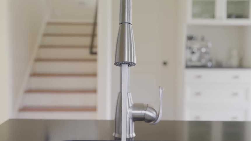 A high quality water faucet in a kitchen is turned on and flowing continuously into the sink below