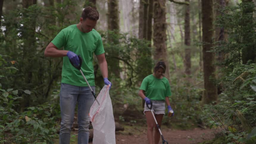 A man and woman are picking up trash in a forest