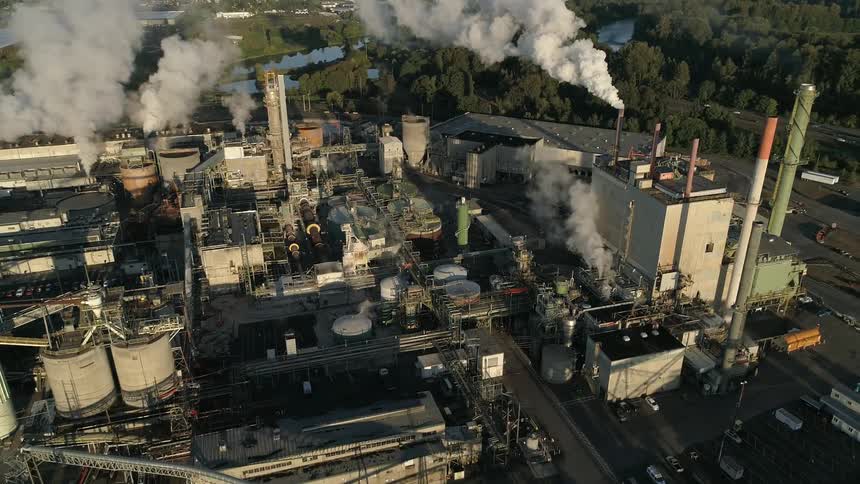 Smoke billows from large smokestacks at a massive refinery facility