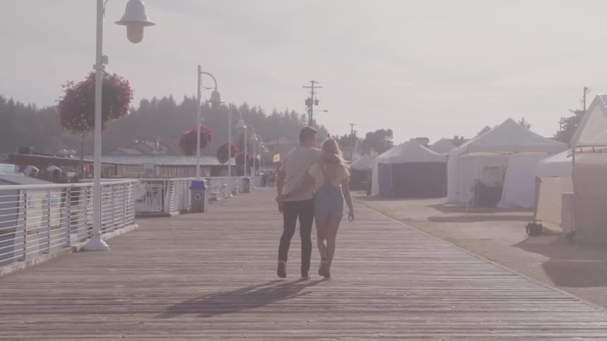 Blonde girl and boy holding each other stroll along on the promenade on a sunny day