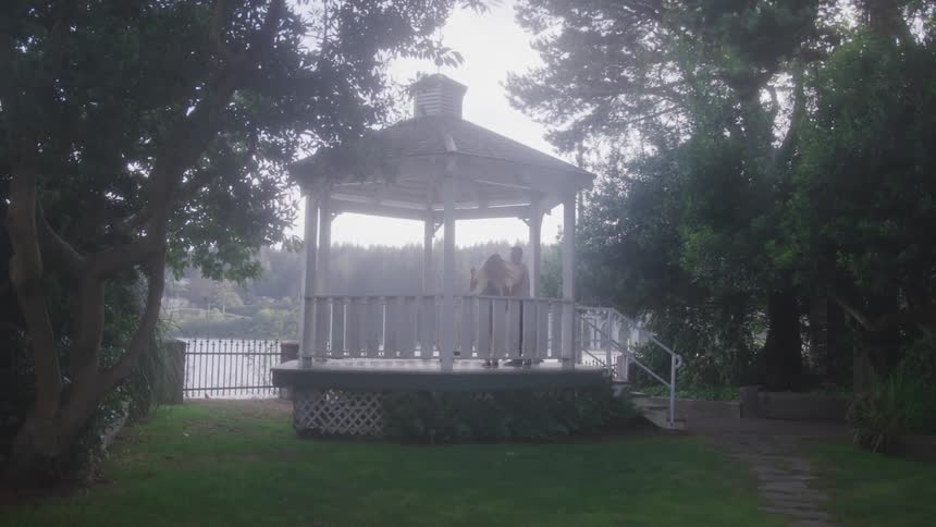 A man and woman dance in a white gazebo surrounded by green trees