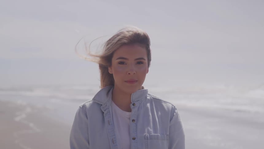 Woman stands on beach with wind ruffling hair