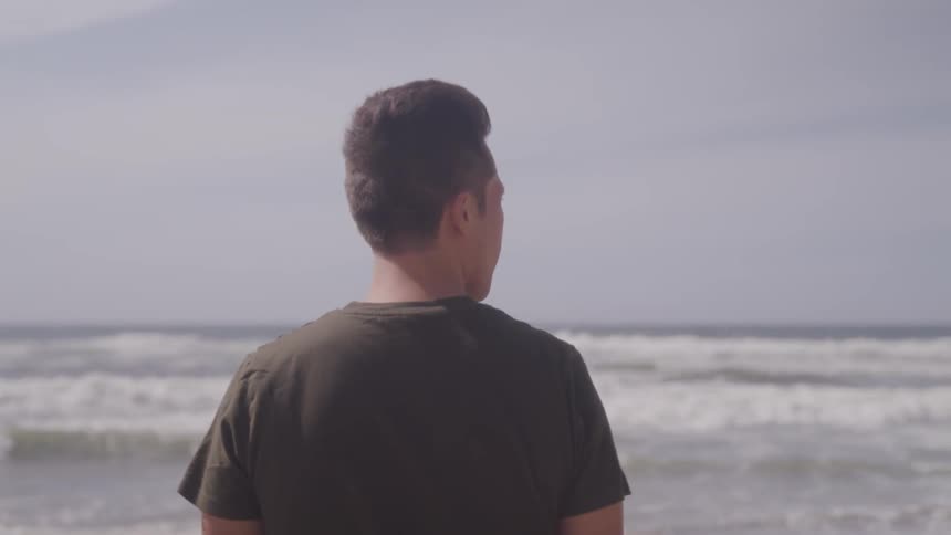A young man stands and looks out at the ocean