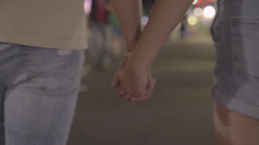 A man and woman hold hands while walking down a boardwalk at night