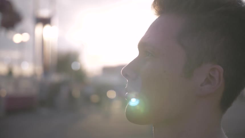 A young male stands outdoors looking upward as the sun shines brightly in the sky behind him