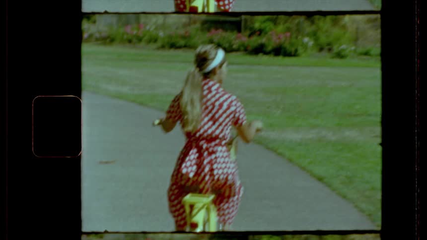 A female in a red dress with white dots rides along a path on a brightly colored bicycle