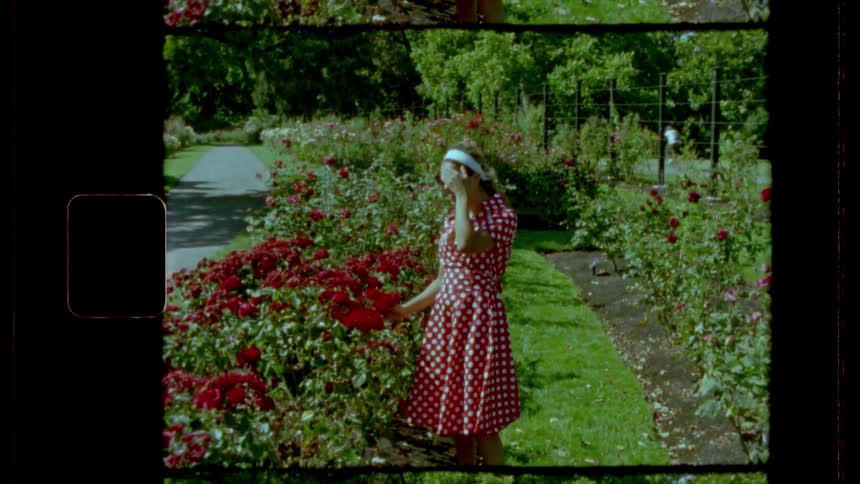 Film footage of a young woman looking at flowers and then waving at the camera