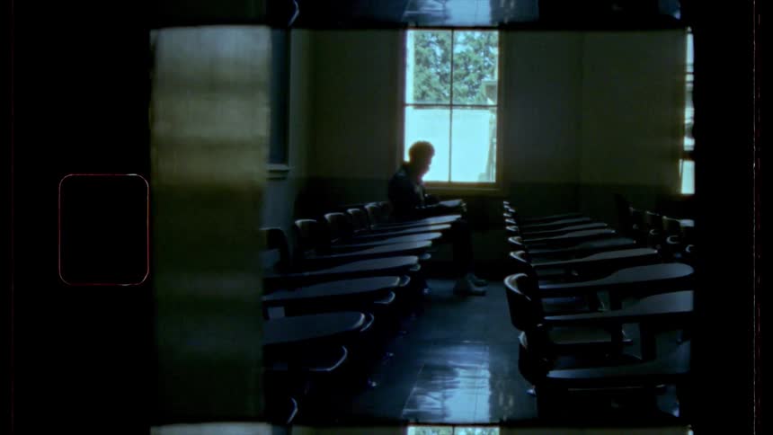 Film footage of a male sitting in a desk in a classroom