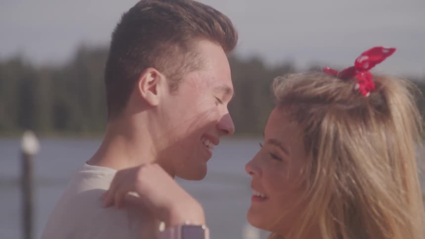 A young man and woman smile as they kiss and them embrace while standing outdoors